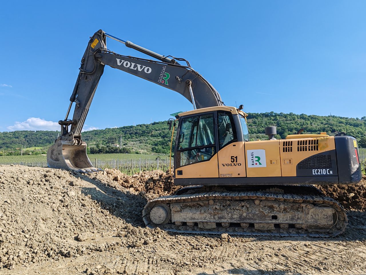 Yellow Volvo excavator working on a construction site in a hilly terrain under a clear blue sky.